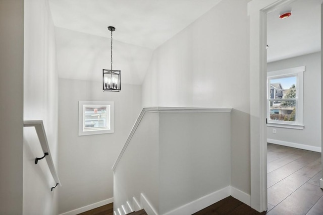 stairway with vaulted ceiling, wood finished floors, baseboards, and a chandelier