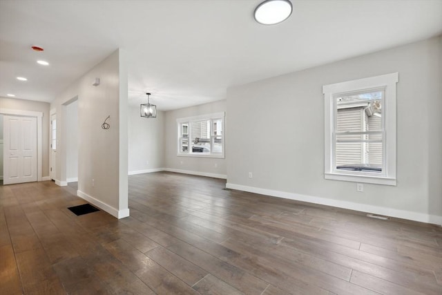 unfurnished living room with dark wood-type flooring, a notable chandelier, recessed lighting, and baseboards