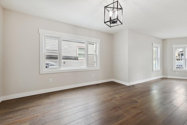 empty room featuring baseboards, dark wood-style flooring, and a chandelier