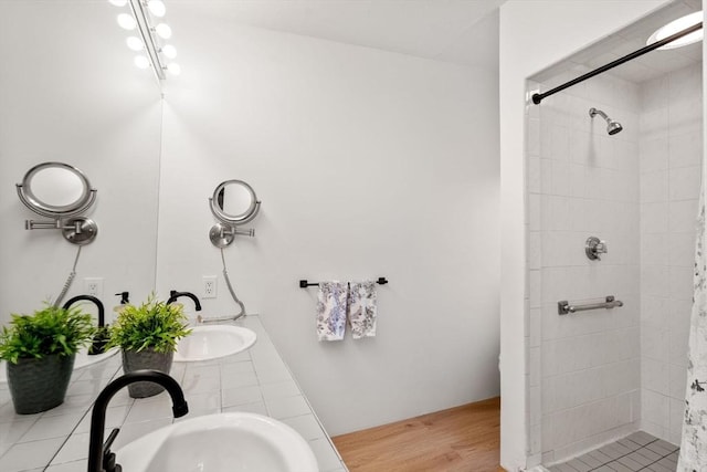 bathroom with wood finished floors, tiled shower, and a sink