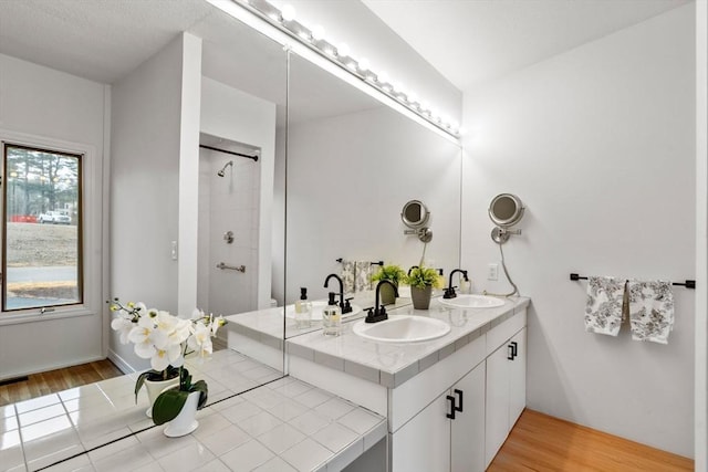 full bathroom with double vanity, wood finished floors, tiled shower, and a sink