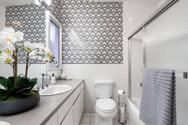 full bathroom with toilet, shower / bath combination with glass door, tile walls, tile patterned flooring, and vanity