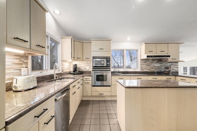 kitchen with a sink, under cabinet range hood, cream cabinets, appliances with stainless steel finishes, and tile patterned flooring