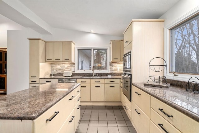 kitchen featuring lofted ceiling, light tile patterned flooring, a sink, stainless steel appliances, and cream cabinetry