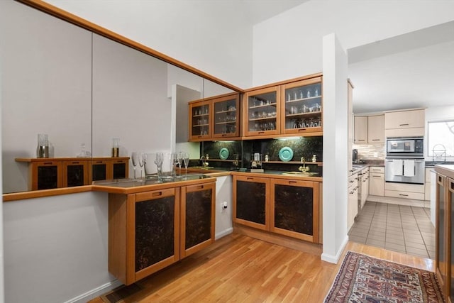 kitchen featuring oven, light wood-style flooring, decorative backsplash, glass insert cabinets, and built in microwave