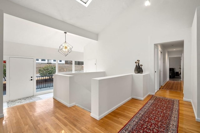 hallway featuring baseboards, high vaulted ceiling, and wood finished floors