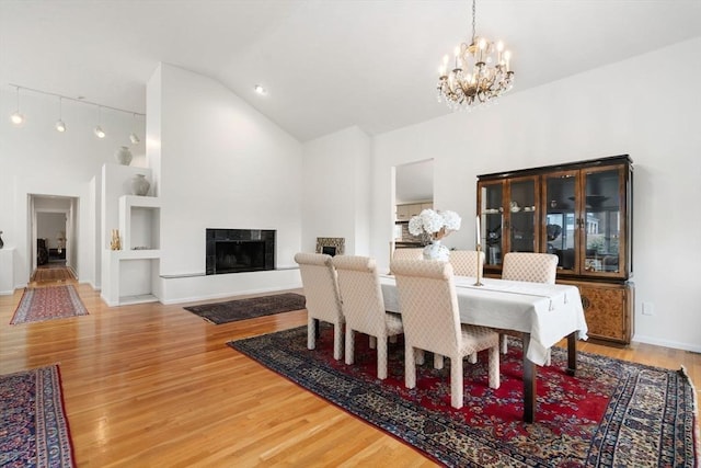 dining space featuring high vaulted ceiling, wood finished floors, a fireplace, baseboards, and a chandelier