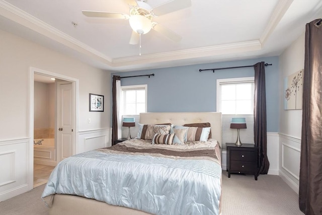 bedroom featuring light carpet, ensuite bath, a tray ceiling, and wainscoting