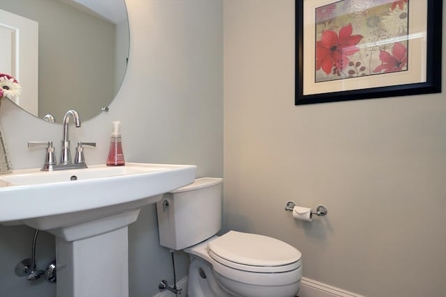 half bathroom featuring baseboards, a sink, and toilet