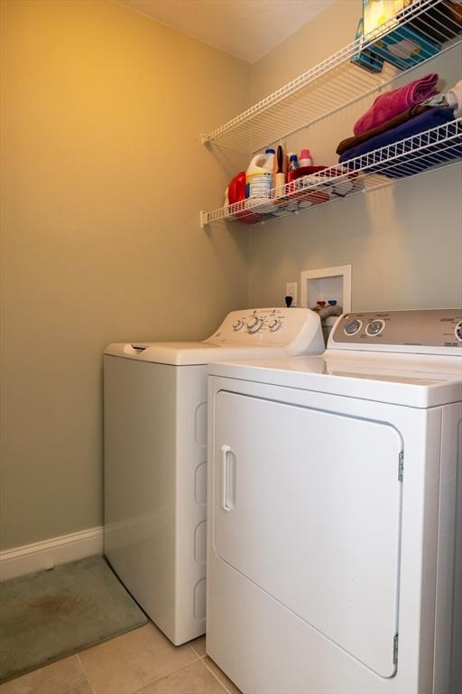 clothes washing area with laundry area, light tile patterned floors, baseboards, and separate washer and dryer