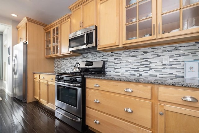 kitchen featuring dark stone counters, appliances with stainless steel finishes, glass insert cabinets, and tasteful backsplash