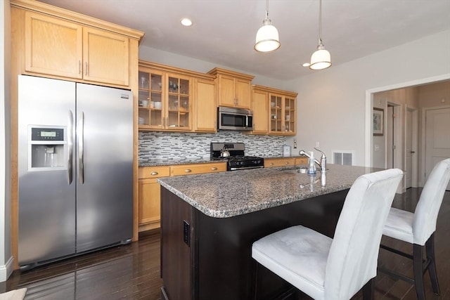 kitchen featuring an island with sink, glass insert cabinets, dark stone countertops, stainless steel appliances, and a sink