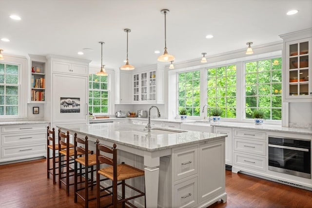 kitchen featuring pendant lighting, sink, white cabinetry, an island with sink, and stainless steel oven