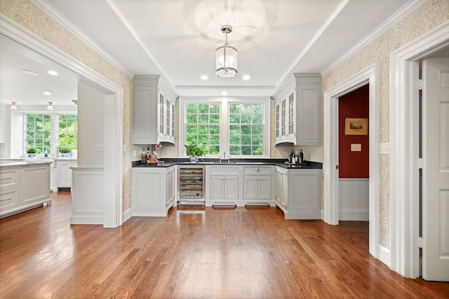 kitchen with hanging light fixtures, crown molding, beverage cooler, and light hardwood / wood-style floors