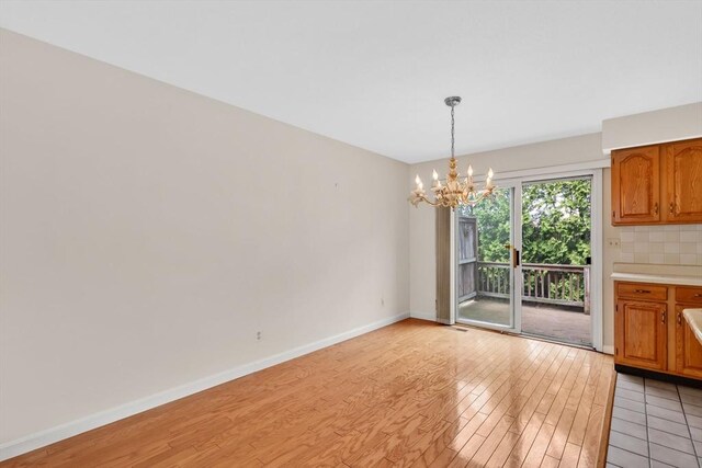 unfurnished dining area with light wood-type flooring, baseboards, and a chandelier