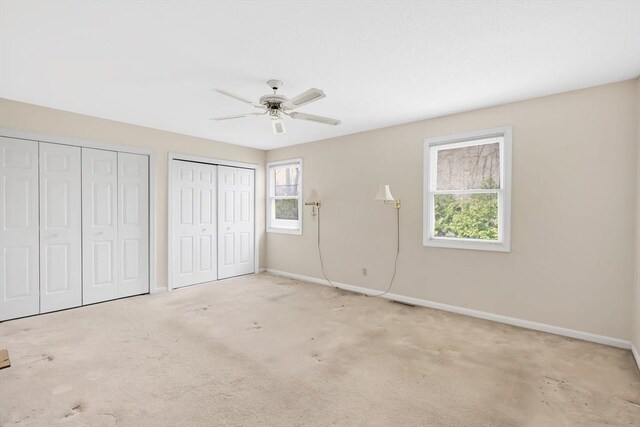 unfurnished bedroom featuring two closets, baseboards, ceiling fan, and carpet flooring