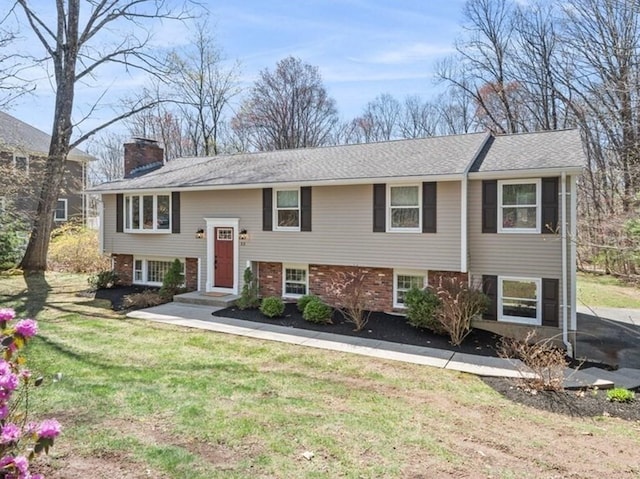 raised ranch featuring a front yard, brick siding, and a chimney