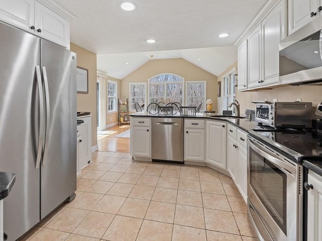 kitchen with stainless steel appliances, dark countertops, a sink, white cabinetry, and a peninsula