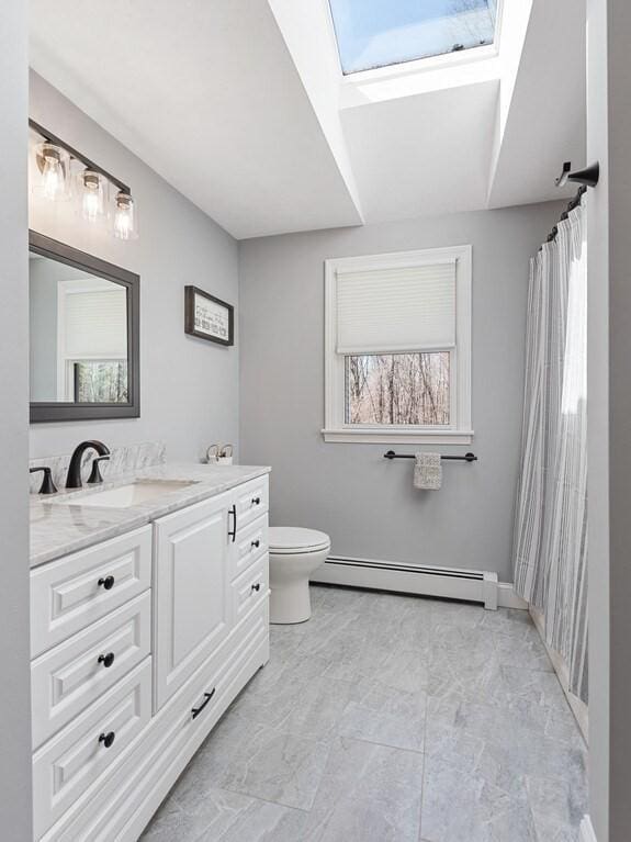 full bathroom with a skylight, marble finish floor, baseboard heating, toilet, and vanity