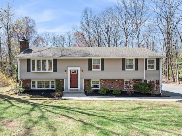 raised ranch with a chimney, brick siding, and a front lawn