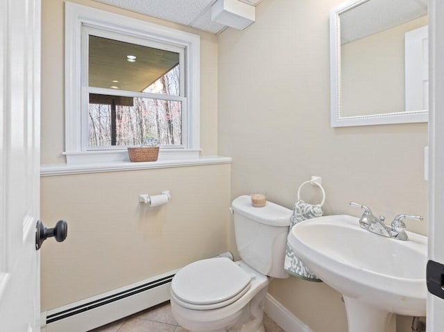 half bathroom with a baseboard heating unit, a sink, tile patterned floors, toilet, and baseboards