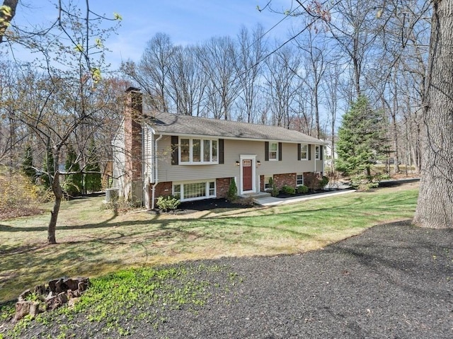 bi-level home featuring a chimney, a front yard, and brick siding