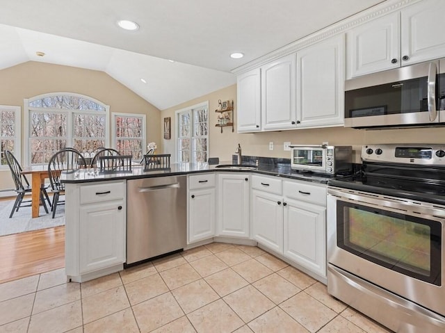 kitchen with stainless steel appliances, a sink, white cabinetry, a peninsula, and lofted ceiling