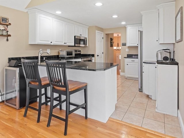 kitchen with stainless steel appliances, a kitchen bar, a peninsula, white cabinetry, and dark countertops