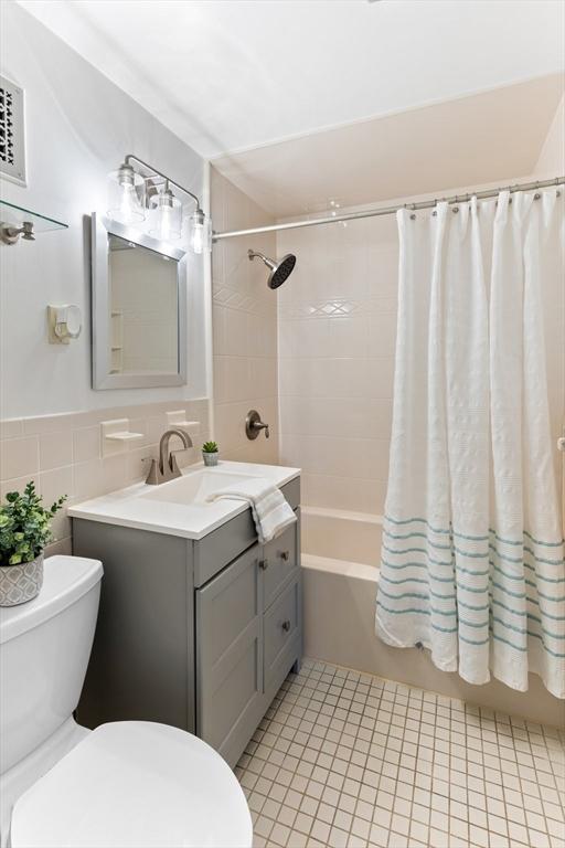 full bathroom featuring tile walls, shower / bath combination with curtain, tile patterned flooring, vanity, and toilet