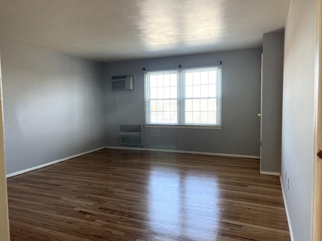 empty room featuring baseboards, wood finished floors, and a wall mounted air conditioner