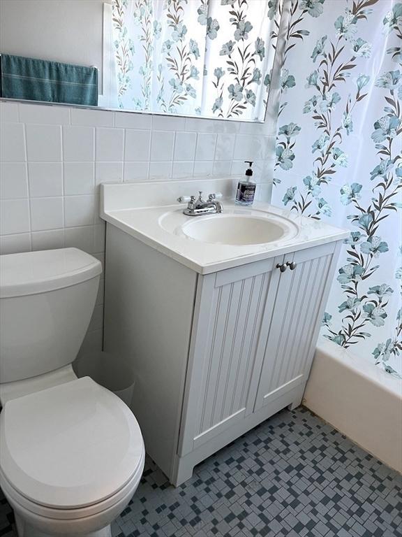 bathroom featuring tile walls, toilet, wainscoting, vanity, and wallpapered walls