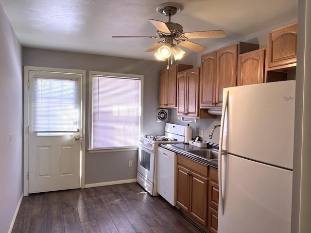 kitchen with white appliances, a sink, a ceiling fan, baseboards, and dark wood finished floors