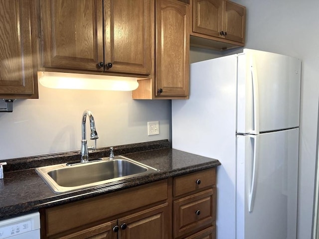 kitchen featuring dark stone counters, white appliances, brown cabinetry, and a sink