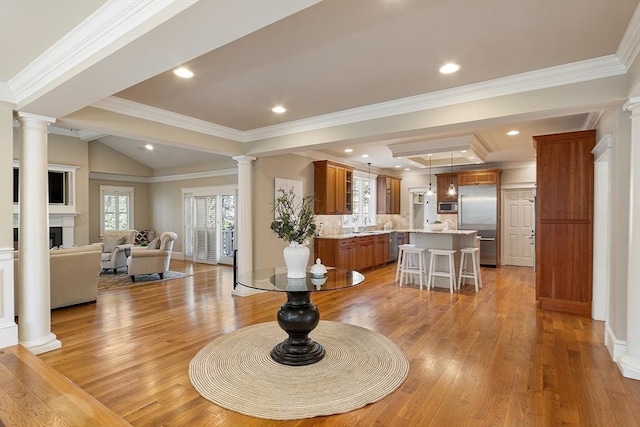 living area featuring a healthy amount of sunlight, a fireplace, light wood-type flooring, and ornate columns