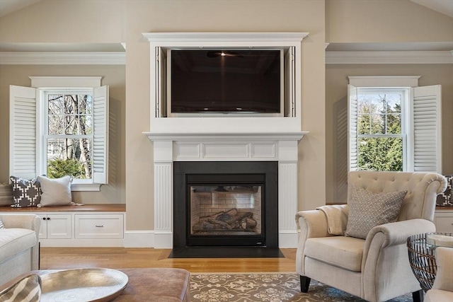 living area featuring vaulted ceiling, a fireplace with flush hearth, light wood finished floors, and ornamental molding