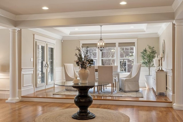 dining room featuring a notable chandelier, hardwood / wood-style flooring, wainscoting, and ornate columns