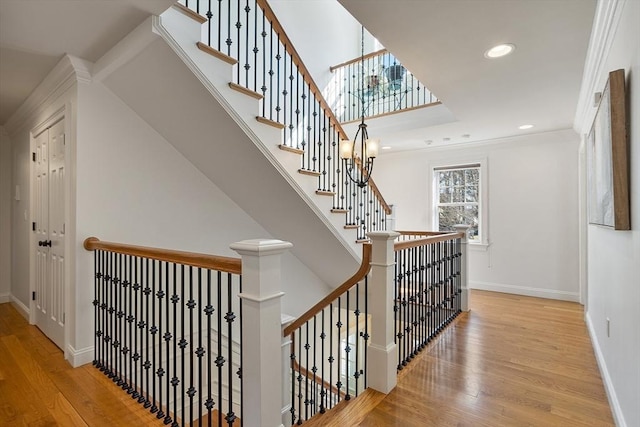 stairway with wood finished floors, baseboards, a high ceiling, recessed lighting, and crown molding