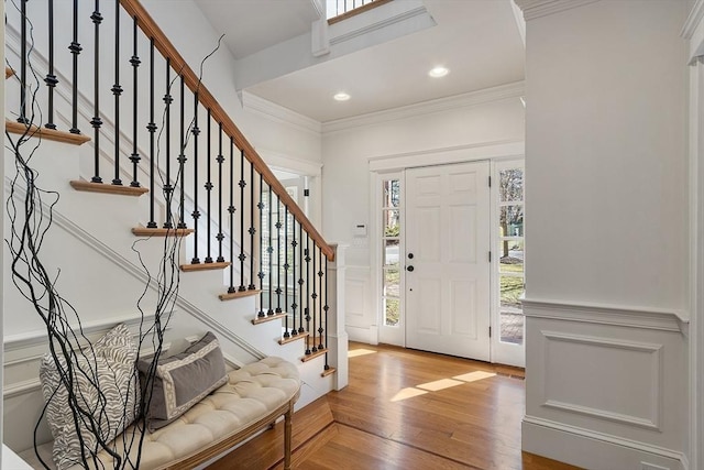 foyer entrance featuring crown molding, a wainscoted wall, recessed lighting, wood finished floors, and a decorative wall