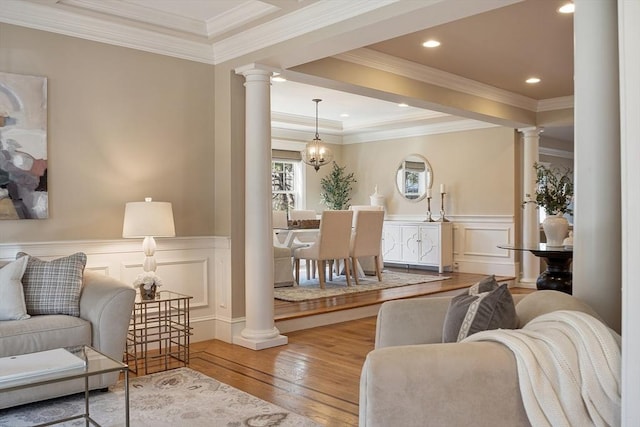 living area with hardwood / wood-style flooring, crown molding, a wainscoted wall, and ornate columns