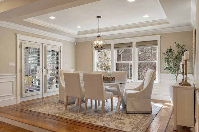 dining area featuring a tray ceiling, wood finished floors, wainscoting, and a decorative wall