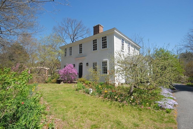 view of side of home with fence, a yard, and a chimney