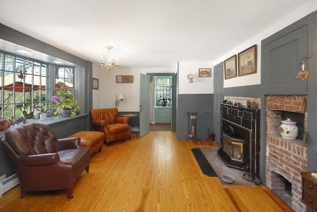 living area with light wood-type flooring, a wood stove, a notable chandelier, and a fireplace