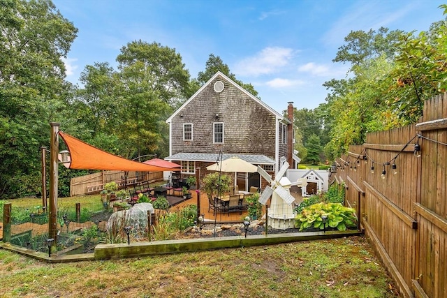 rear view of house featuring a chimney, a garden, a fenced backyard, and a wooden deck