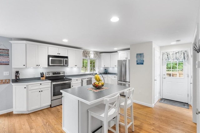 kitchen with stainless steel appliances, light wood-type flooring, white cabinets, and a breakfast bar