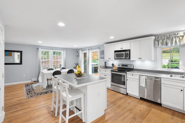 kitchen with a breakfast bar area, light wood-style flooring, a kitchen island, white cabinetry, and appliances with stainless steel finishes