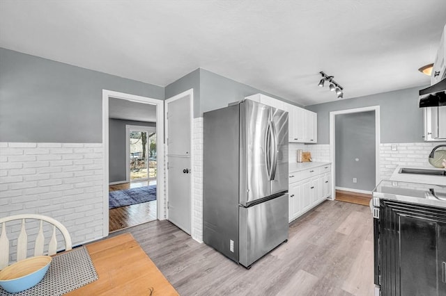 kitchen featuring sink, light hardwood / wood-style floors, stainless steel refrigerator, and white cabinets