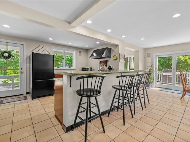 55 Dwight St, Dedham, MA 02026 - kitchen featuring freestanding refrigerator, light tile patterned floors, wall chimney exhaust hood, a kitchen breakfast bar, and recessed lighting