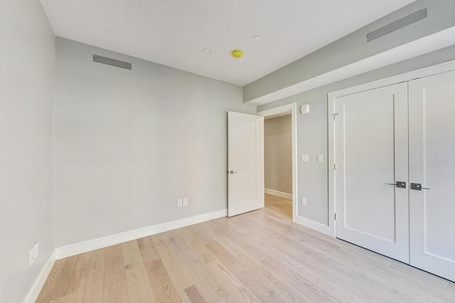 unfurnished bedroom featuring light wood finished floors, a closet, visible vents, and baseboards