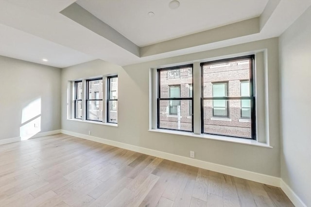 spare room featuring a raised ceiling, light wood-style flooring, and baseboards