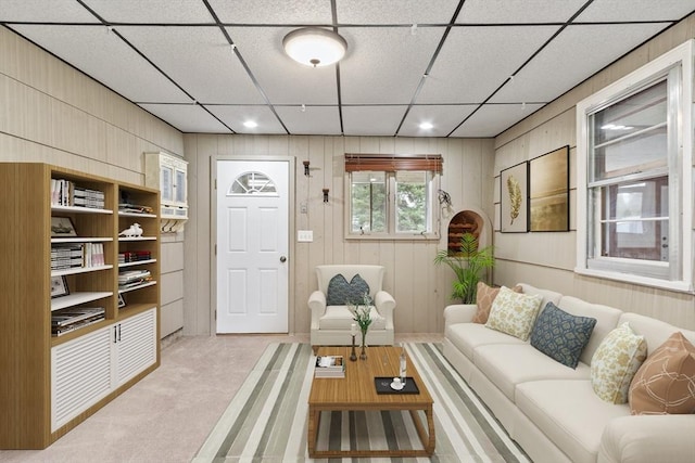 living room featuring light colored carpet, wood walls, and a drop ceiling